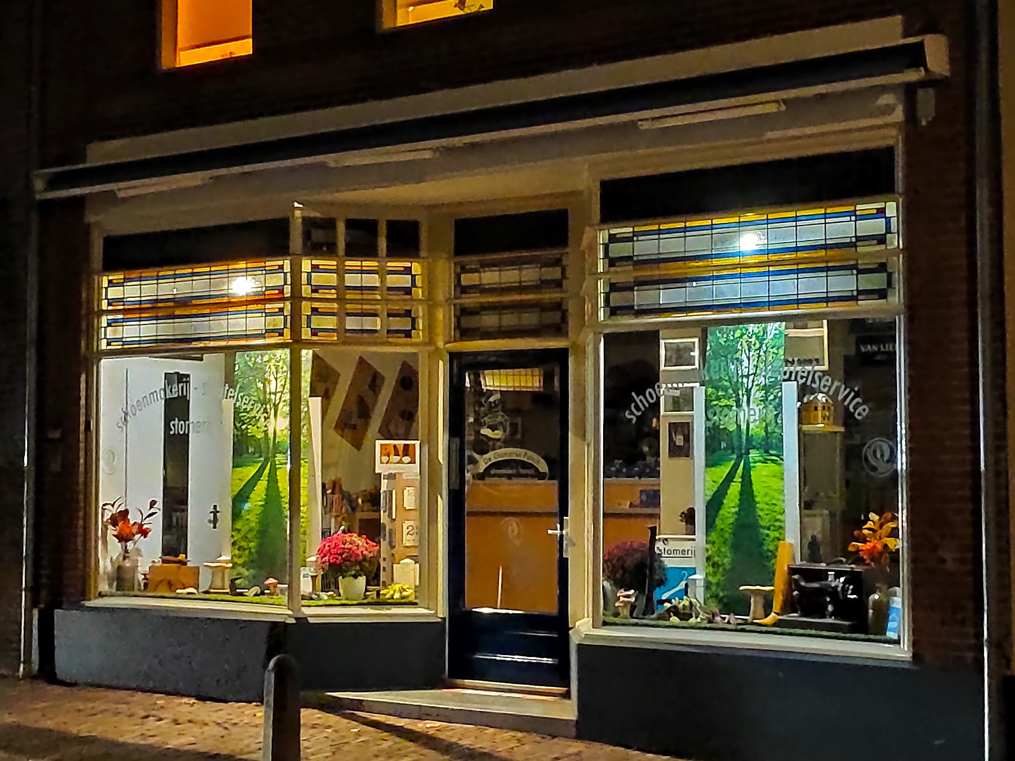 De etalage van de schoenmakerij in de avond, met verlichte ramen en de deur in het midden
